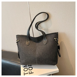 Detail of contrast stitching and golden hardware on a dark grey denim tote bag