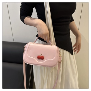 Detailed view of pink crossbody bag featuring 3D cherry accents and top handle
