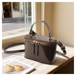 Detail of dark brown patent leather square bag with gold hardware on wooden surface