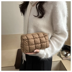 Close-up of brown quilted puffy makeup bag texture held by model in white sweater