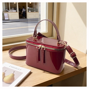 Detailed view of glossy burgundy patent leather box bag with gold double zip closure