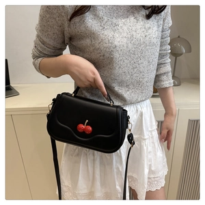 Close-up of black PU leather handbag featuring a 3D red cherry metal buckle detail