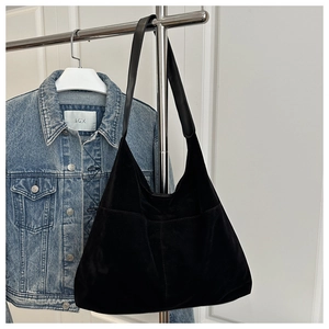 Détail d'un sac cabas noir en daim avec large bandoulière suspendu à côté d'une veste en jean