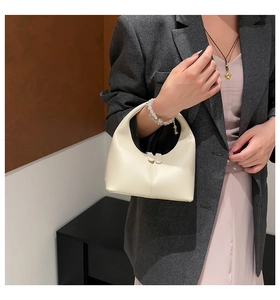 Detail of a cream crescent handbag featuring vertical stitching and dual zippers