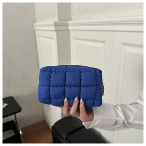 Modelo sostiene un neceser acolchado azul real con diseño de cuadros y cremallera metálica