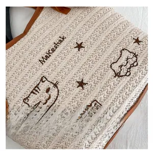Détail du sac cabas en paille tressée avec broderies cartoon et poignées marron