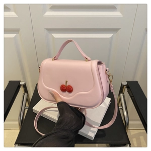 Detailed close-up of pink cherry handbag with gold metal stem on a white book