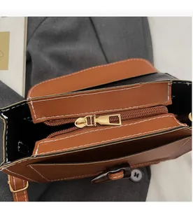 Detail view of smooth golden zipper and white contrast stitching on brown crossbody bag