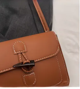 Close-up of brown crossbody bag featuring white stitching and unique horn buckle detail