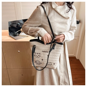 Détails des broderies de chats et des anses en cuir noir sur un sac fourre-tout