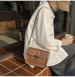 Detail of a brown leather crossbody bag with white stitching in a lifestyle setting