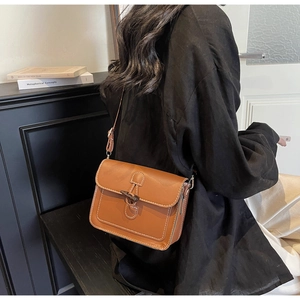 Detailed side view of brown leather crossbody bag with horn buckle and contrast stitching
