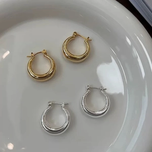 Detailed view of polished thick gold and silver hoop earrings on a ceramic dish