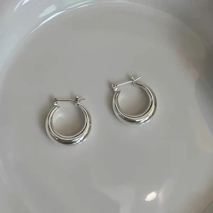 Close-up of polished silver hoop earrings with high-shine finish on a white ceramic plate