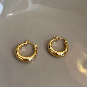 Detailed close-up of chunky gold hoop earrings with a polished mirror finish on gray tray