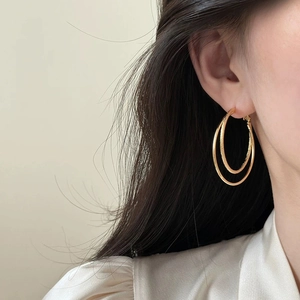Detail of model wearing gold double hoop earrings with polished and frosted metal textures