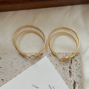 Detail of double-layer gold hoop earrings with polished outer and frosted inner texture