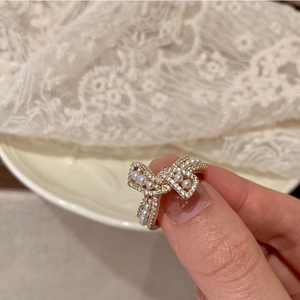 Λεπτομέρεια χρυσού δαχτυλιδιού με φιόγκο, πέρλες και ζιργκόν φορεμένο στο χέρι