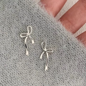 Elegant silver ribbon bow stud earrings for women on a grey knit sweater background
