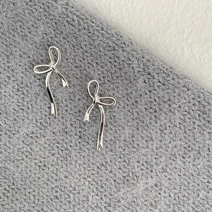 Elegant silver ribbon bow earrings on soft grey knit fabric in a top-down view