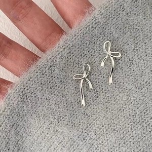 Close-up of elegant silver ribbon bow earrings displayed on soft grey knit fabric