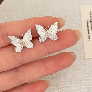 Elegant butterfly stud earrings with pearl shell inlay and sparkling crystals held by hand