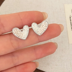 Macro detail of heart-shaped silver earrings with textured white shell inlay