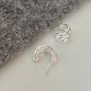 Macro detail of silver layered C-shaped stud earrings with textured metallic finish