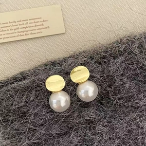 Detail shot of pearl earrings with gold metal discs on a gray textured fabric