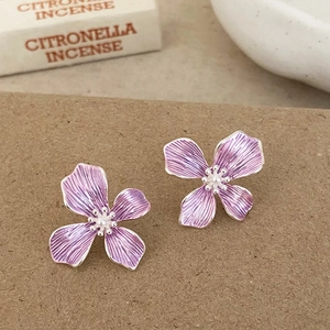 Macro shot of purple flower earrings with pearl centers and silver edges on brown paper