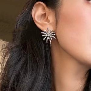 Détail macro d'une boucle d'oreille feu d'artifice argentée avec rayons et cristal sur l'oreille