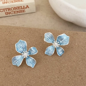 Close-up of light blue flower stud earrings with central pearl and silver metallic texture