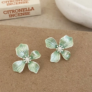 Macro view of green enamel flower earrings with a small pearl center on craft paper
