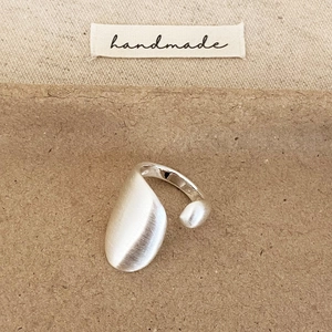 Bague ouverte argentée mate brossée irrégulière sur un fond kraft fait à la main