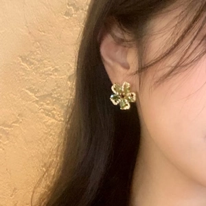 Elegant gold flower stud earrings with green zircon petals worn on a female ear
