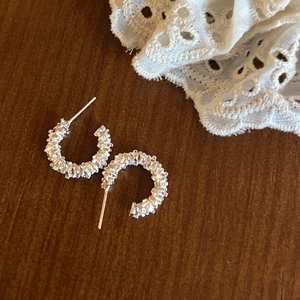 Detail of silver C-shape hoop earrings with crushed silver texture on wooden base