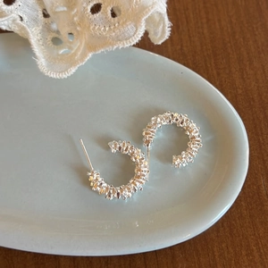 Detail of silver C-shape earrings with textured crushed silver surface on lace background