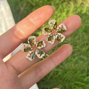 Macro detail of olive green zircon flower earrings held on fingers with outdoor background