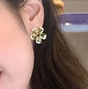 Close-up of model wearing floral zircon stud earrings with green petals and golden base