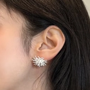 Detailed close-up of a silver zircon dandelion earring worn on a model ear lobe
