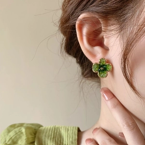 Detailed close-up of clover flower stud earrings with green crystals and gold cord edge
