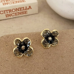 Detail of flower stud earrings with gold frames and dark crystals on earthy paper