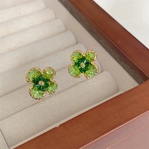 Detailed macro view of four-leaf clover flower earrings with green crystal inlay