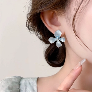Close-up of blue flower earrings with textured petals and center pearl on model's ear