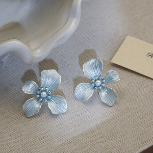 Detailed view of light blue flower stud earrings with delicate pearls on linen fabric