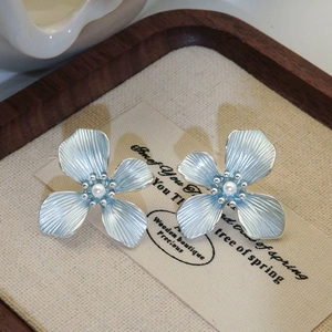 Close-up of blue four-petal flower earrings with central pearl on rustic wooden tray