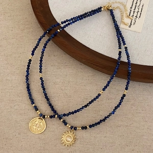 Collana a doppio strato in lapis e ciondoli a sole dorato su vassoio in legno rustico