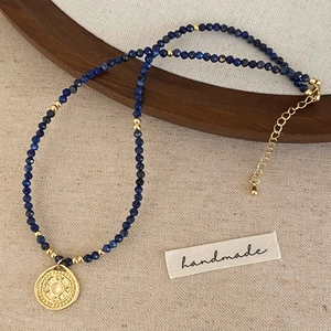 Detailaufnahme der handgefertigten Kette mit Lapislazuli-Perlen und goldenem Medaillon