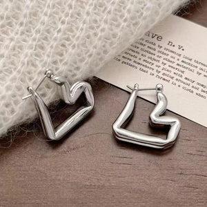 Macro shot of silver irregular heart earrings on a wooden stand with soft knit background
