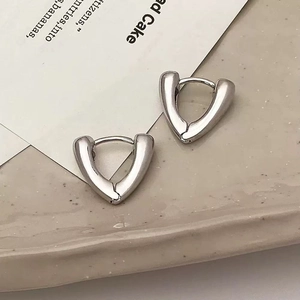 Close-up of minimalist silver triangular hoop earrings on a decorative ceramic tray